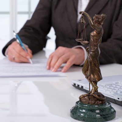 person signing document with lady justice statue on desk